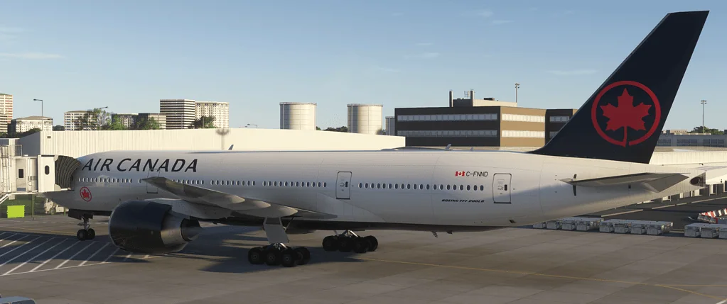 Air Canada Boeing 777 aircraft parked on airport tarmac with cityscape background.